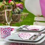 Ein bunt geschmückter Tisch mit Herzluftballons und passenden Servietten steht im Garten, alles ist hübsch dekoriert und die Gäste können kommen.