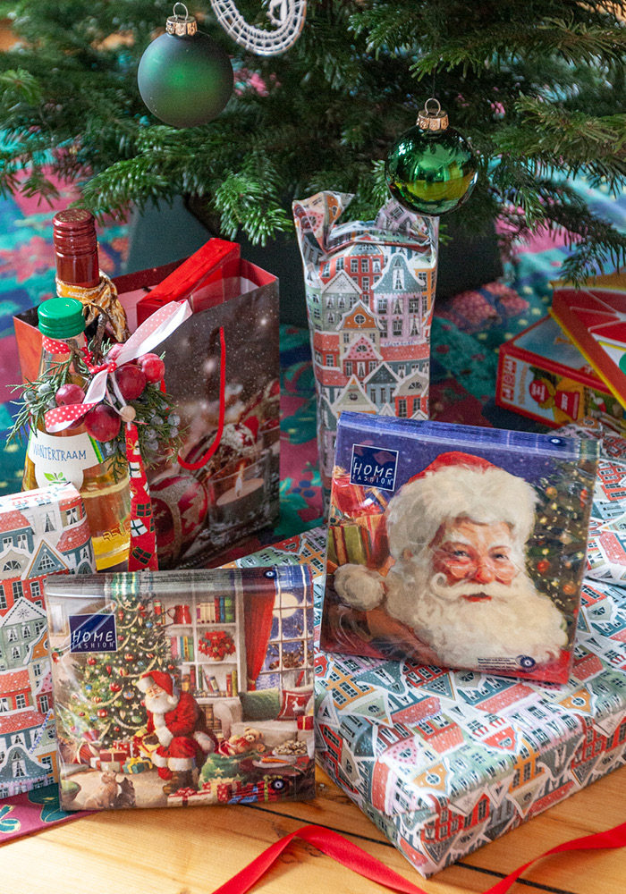 Geschenke über Geschenke liegen unter dem Weihnachtsbaum. Da fällt es kaum auf dass der Weihnachtsmann auf Serviette bedruckt hervor schaut.