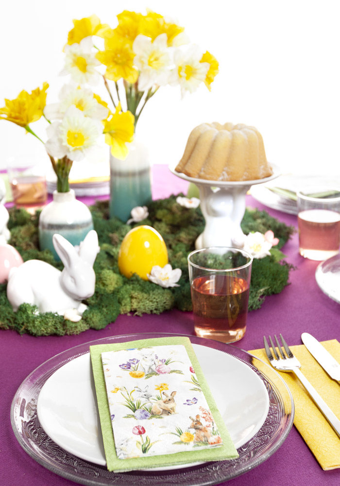 Ein bunt gedeckter Ostertisch mit gelben Narzissen wurde auf purple farbiger Tischdecke dekoriert.