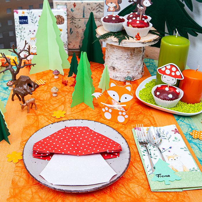 Tischdekoration für kinder mit servietten die zum fliegenpilz gefaltet sind und verschiedenen dekorationselementen